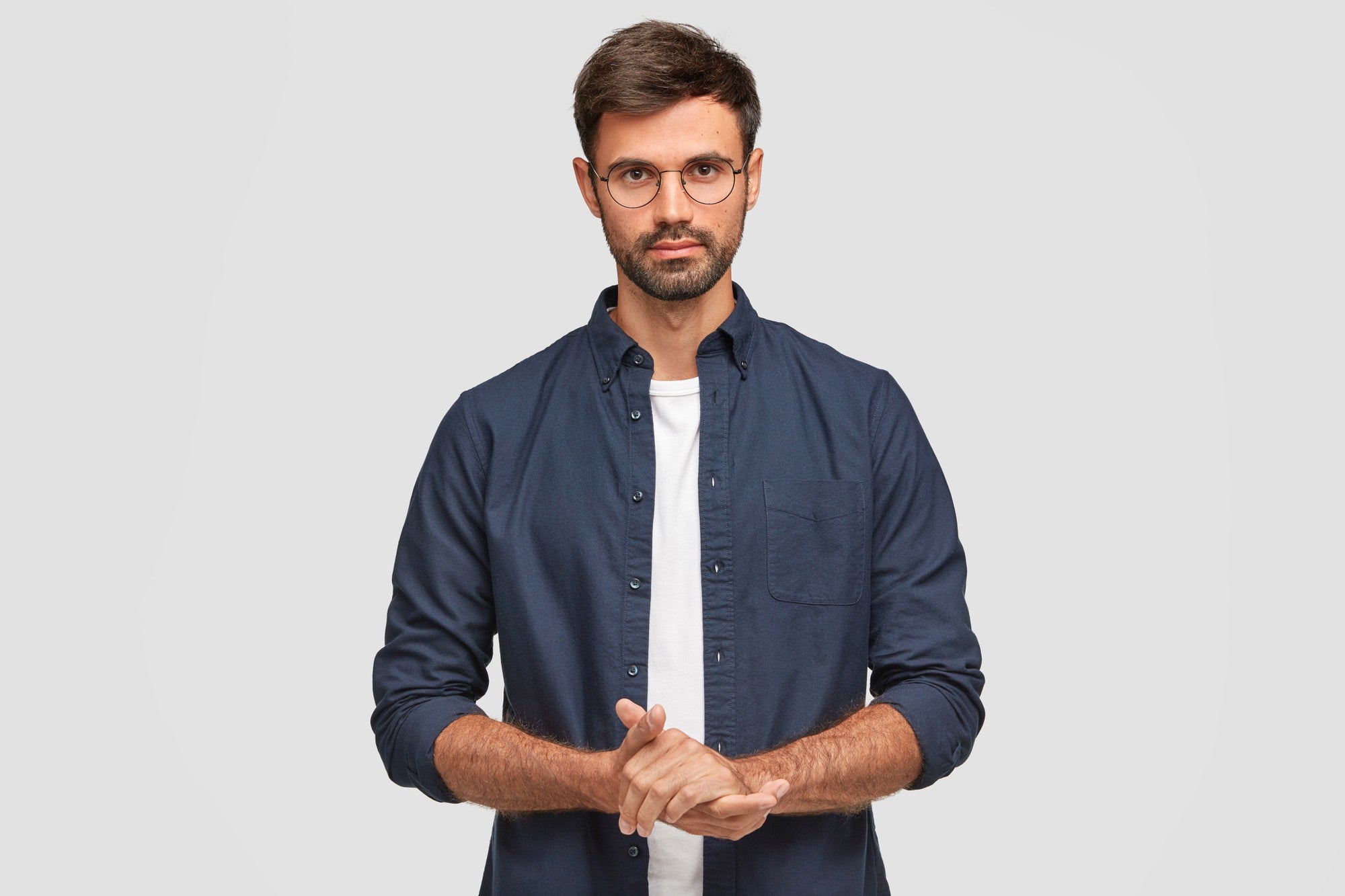 files/waist-up-portrait-handsome-serious-unshaven-male-keeps-hands-together-dressed-dark-blue-shirt-has-talk-with-interlocutor-stands-against-white-wall-self-confident-man-freelancer.jpg